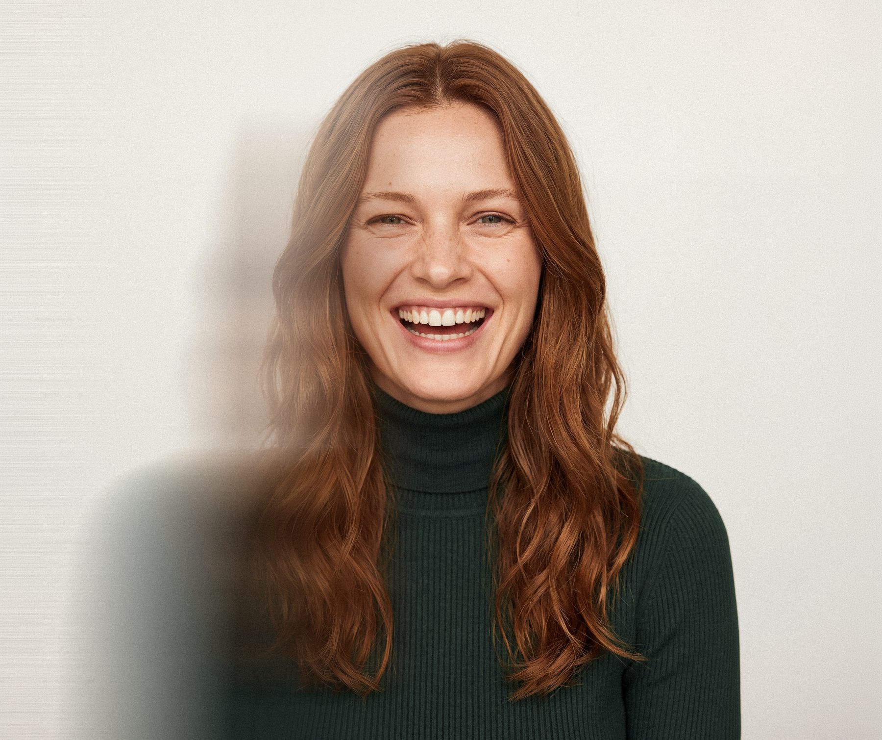 A woman laughing, red hair, dark green sweater